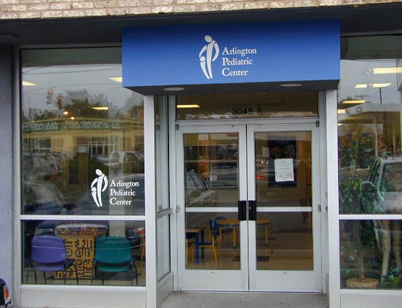 arlington pediatric center entrance with their logo on display on the awning and glass window. the logo intends to depict an adult patting a small child on the head, but due to a terrible design it can be misconstrued to look sexual in nature, certainly not what the business intended